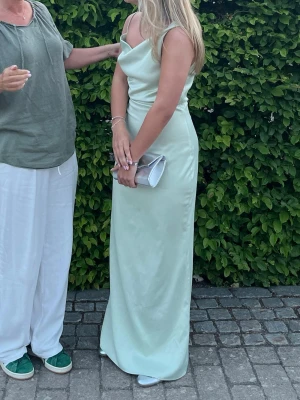 Ljusgrön långklänning med slits - Elegant ljusgrön klänning, den har en slits på sidan och är tillverkad i ett glansigt, satinliknande material som ger en lyxig känsla. Perfekt för speciella tillfällen så som bal, middag eller bröllop💝
