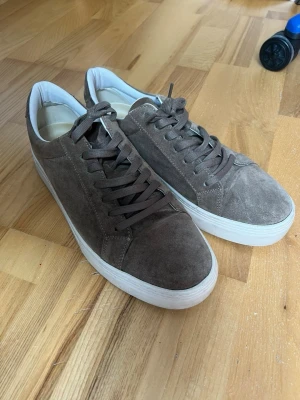 Vagabond - Snygga bruna sneakers i mocka med klassisk låg profil och vit, tjock sula. Skorna har bruna skosnören och en stilren design som passar till det mesta. Insidan är fodrad i vitt tyg för extra komfort. Perfekta för dig som gillar en clean och enkel look.