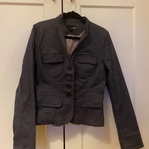 Mörkblå kavajjacka från H&M - Snygg mörkblå kavajjacka från H&M med fyra fickor framtill och markerad midja. Jackan har knappar hela vägen och lång ärm. Materialet är bomull och jackan har en klassisk krage.💕