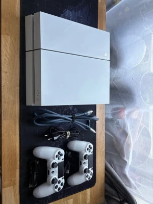 Vit PlayStation 4 med två kontroller - Säljer en stilren vit PlayStation 4 med två matchande DualShock 4-kontroller. Konsolen har en kantig design och är tillverkad i plast. HDMI-kabel och laddningskablar till handkontrollerna ingår. Perfekt för gamingkvällar och multiplayer.