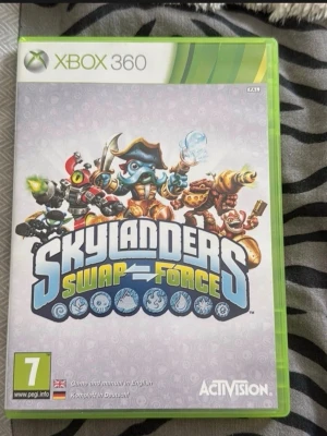 Skylanders Swap Force Xbox 360 spel - Skylanders Swap Force till Xbox 360 är ett actionäventyrsspel där du kan mixa och matcha olika figurer för att få nya krafter. Omslaget är grönt med färgglada karaktärer och spelets logga i blått och vitt. Perfekt för dig som gillar fantasy och samlarspel.
