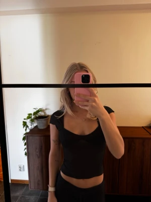 Svart croppad topp med öppen rygg - Snygg svart croppad topp med korta ärmar och en fin öppen ryggdetalj. Toppen har en tight passform och är perfekt för dig som vill ha en trendig och enkel look. Passar till både jeans och kjol.