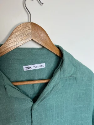 Grön linneskjorta från Zara - Snygg grön skjorta från Zara i 100% linne. Skjortan har korta ärmar, klassisk krage och knäppning framtill med vita knappar. Perfekt för en avslappnad och trendig look. Storlek M. Mycket fint skick