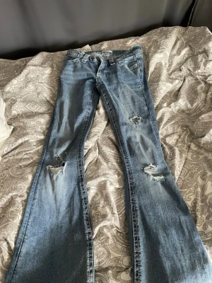Blåa bootcut jeans från Gina tricot young - Ett par blåa bootcut jeans med hål i från Gina tricot Young. Storlek xs 14+. Det slitna i hålen har försvunnit lite och lite slitet längst ner men annars är de i mycket bra skick utan skavanker 