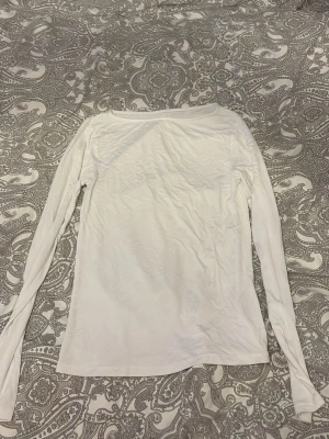 Vit långärmad topp med båtringning - En enkel och stilren vit långärmad topp med båtringad hals. Tillverkad i ett mjukt och tunt material som känns skönt mot huden. Perfekt att matcha med jeans eller kjol för en clean look.
