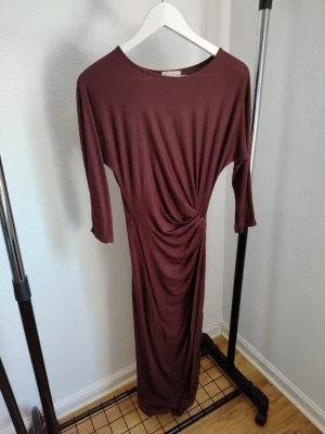 Två långärmade maxiklänningar - Säljer två maxiklänningar, en i vinröd med drapering i midjan och trekvartsärm, samt en beige ribbad med rund ringning och långa ärmar. Båda har en smal passform och är tillverkade i mjukt, stretchigt material.