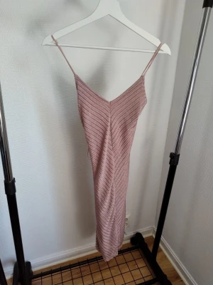 Rosa stickad klänning med smala axelband - Säljer en rosa stickad klänning med smala axelband och v-ringad front. Klänningen är lång och har ett diskret randigt mönster i stickningen. Perfekt för dig som gillar en enkel och stilren look.