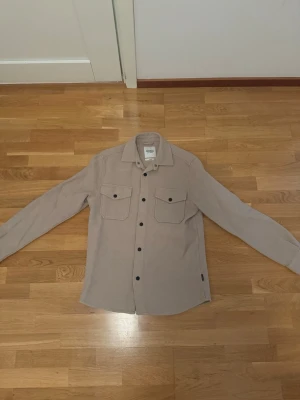 Beige overshirt från Dobber - Stilren beige overshirt från Dobber med två bröstfickor och svarta knappar. Helt oanvänd på grund av att den är för stor för mig.