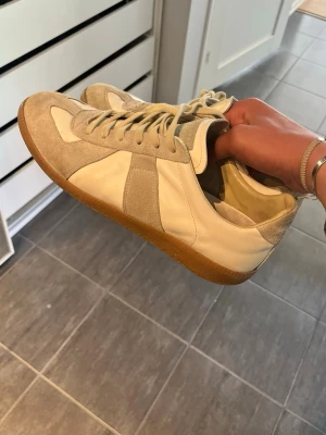 Mm Gats - Säljer ett par gats sneakers i vitt och beige. Skorna har ovandel i mocka och läder, med gummisula och vita snören. Snygg retrostil som passar till det mesta och ger en clean look.