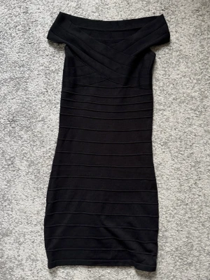 Svart offshoulder kort klänning - Säljer en svart, tight offshoulder klänning med ribbade horisontella ränder. Klänningen har en kroppsnära passform och är axelbandslös, perfekt för dig som gillar en stilren och trendig look.