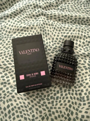 Valentino Uomo Born In Roma Intense - Valentino Uomo Born In Roma Intense är en lyxig parfym i en mörk, nitar-inspirerad glasflaska med svart och rosa detaljer. Flaskan har en unik, kantig form och känns riktigt exklusiv. Doften är en Eau de Parfum Intense och flaskan rymmer 50 ml.