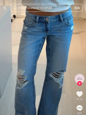 Blå slitna low waist jeans Gina Tricot - Säljer ett par ljusblå low waist jeans från Gina Tricot med lös passform och stora slitningar på båda benen. Jeansen har klassisk femficksmodell och vida ben. Perfekta för en avslappnad och trendig look.