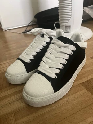 NUMERIŚ Svartvita Chunky Platform Sneakers  - Säljer ett par helt nya, oanvända låga sneakers från NUMERIŚ i en stilren svartvit färgkombination. De har en riktigt snygg tjock platåsula med en unik räfflad/sågtandad undersida och supertrendiga, extra breda vita skosnören.