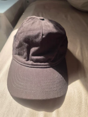Mörkbrun klassisk bomullskeps h&m - Snygg mörkbrun keps i klassisk modell med böjd skärm och justerbart spänne bak. Tillverkad i mjuk bomull med ventilationshål på sidorna för extra komfort. Perfekt accessoar för en avslappnad och stilren look.