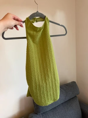 Grön ribbad halterneck topp - Säljer en snygg ljusgrön halterneck topp med ribbad struktur och knapp i nacken. Toppen är ärmlös och har en tight passform.