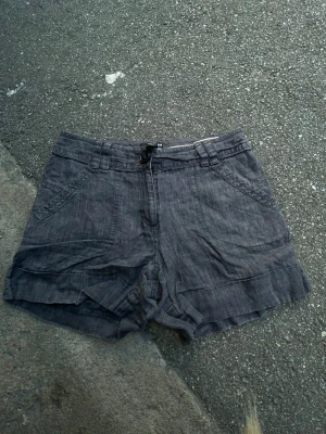 Grå shorts från H&M med fickor - Säljer ett par grå shorts från H&M i storlek 36. De har normal passform, sidofickor och bälteshällor. Materialet känns som bomull och shortsen har en enkel knappstängning framtill. Perfekta för varma dagar!