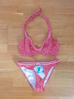 Freya bikini oanvänd  röd med vitt mönster - Snygg röd bikini från Freya med vita prickar och halterneck-band. Överdelen har bygel och knyt i nacken, medan underdelen har klassisk bikini-modell. Materialet är 80% polyamid och 20% lycra för skön stretch. Nypris 349 kr per del.