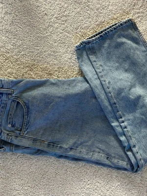 Blå loose fit jeans från Pull&Bear - Säljer ett par ljusblå loose fit jeans från Pull&Bear. Klassisk femficksmodell med raka ben och hög midja. Jeansen är tillverkade i bomull och har en avslappnad passform som ger en cool och trendig look.