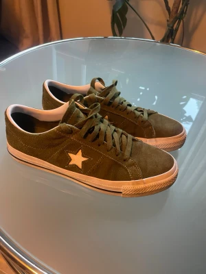 Olivgröna Converse One Star sneakers - Säljer ett par olivgröna Converse One Star sneakers i mocka med vit stjärna på sidan och vit sula. Har använts några gånger men är överlag i bra skick. 