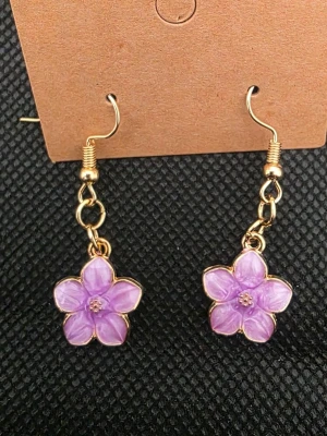 Handgjorda blomformade örhängen - Snygga handgjorda örhängen i form av rosa blommor med guldfärgade detaljer. Blommorna har fem kronblad och en liten detalj i mitten. Perfekta för att ge din look en färgklick och en söt touch. Hängande modell med krok.