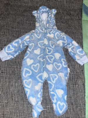 Blå hjärtmönstrad babyoverall - Supermjuk blå overall för baby med vita hjärtan, huva med öron och helkroppsdesign. Perfekt för mysiga stunder hemma. Tillverkad i 100% polyester för extra komfort och värme.