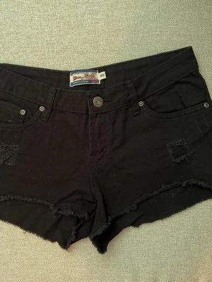 Svarta jeansshorts  - Svarta jeansshorts från Blue Ridge med råa kanter och slitna detaljer framtill. Klassisk femficksmodell med knapp och dragkedja. Perfekta för en avslappnad och cool stil under varma dagar.