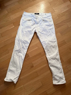 Vita slim fit jeans från Replay - Snygga vita jeans från Replay i slim fit-modell med klassisk femficksdesign. Jeansen har normal midja och raka ben. Tillverkade i ett mjukt bomullsmaterial med lite stretch för extra komfort. Perfekta för dig som vill ha en clean och fräsch look. Defekter som syns på bild, lite färgad där bak! 