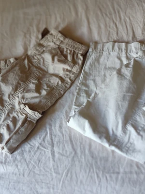 Två par beige shorts i bomull - Säljer två par stilrena shorts i olika beige nyanser. Båda har avslappnad passform och elastisk midja för extra komfort. Tillverkade i mjuk bomull, perfekta för varma dagar. Ena paret har fickor på sidorna och klassisk design.
