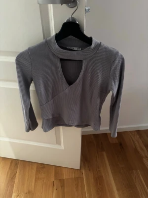 Grå ribbad långärmad topp från ES - Säljer en grå ribbad långärmad topp från ES med cool omlott-design och v-ringad cutout vid halsen. Materialet är mjukt och stretchigt, perfekt för att skapa en snygg look. Passformen är normal och toppen är croppad.