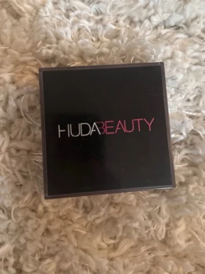 Huda Beauty Easy Bake loose setting powder - Säljer ett Huda Beauty puder i lös form. Färgen är ”banana bread”.  Kommer i en fyrkantig transparent burk med svart lock och logga i vitt och rosa. Pudret är ljust beige och ger en matt finish. Perfekt för att fixera sminket och få en jämn hudton.