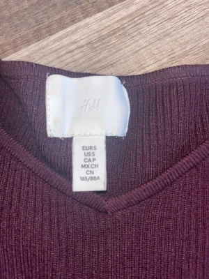 Vinröd ribbad topp från H&M - Säljer en vinröd ribbad topp från H&M med v-ringning och långa ärmar. Toppen har en slim passform och är tillverkad i ett mjukt, stretchigt material som sitter snyggt på kroppen. Perfekt att styla med jeans eller kjol. Köpt för ca 250kr Den är nästan aldrig använd och i väldigt bra skick, kontakta mig för frågor
