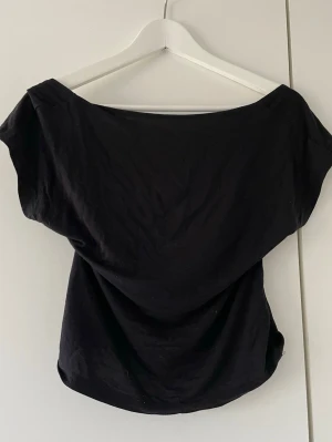 Svart topp - Trendig svart topp som är öppen i ryggen. Toppen har en bred urringning ,vilket ger en cool och avslappnad vibe. Perfekt att matcha med höga jeans eller kjol för en snygg look.