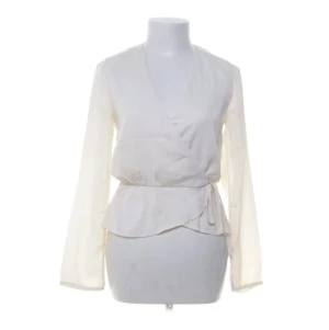 Vit omlottblus från BikBok - Stilren vit omlottblus från BikBok med långa ärmar och knytband i midjan. Blusen har en lätt v-ringning och är tillverkad i ett tunt, mjukt material som ger ett elegant fall. Perfekt att matcha med jeans eller kjol för en trendig look.