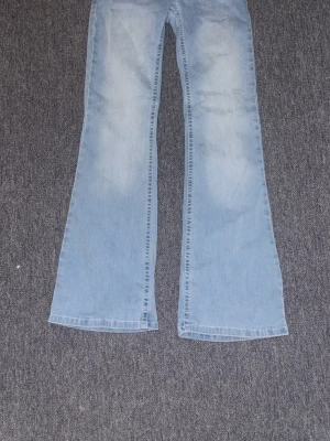 Ljusblå bootcut jeans - Säljer ett par ljusblå bootcut jeans med utsvängda ben och klassisk femficksdesign. Jeansen är ljusblå uttväp. Materialet är mjukt denim och de har en broderad detalj på bakfickan💘💘