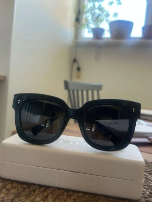 Svarta solglasögon i modellen 08 från Chimi - Snygga svarta solglasögon från Chimi med bred båge och fyrkantig form. Glasen är mörka och bågarna har små silvriga detaljer vid hörnen. Kommer med ett stilrent vitt fodral. Perfekta för en trendig look i solen.