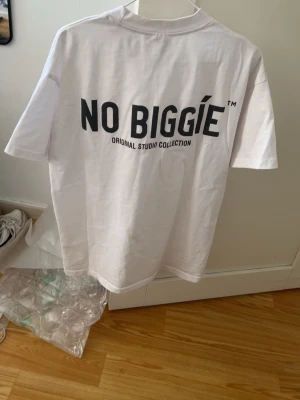 Vit NO BIGGIE t-shirt - Säljer en vit t-shirt från NO BIGGIE med svart tryck både fram och bak. Klassisk rund hals och korta ärmar. Skön passform och tillverkad i mjuk bomull. Perfekt för dig som diggar oversized på gymmet eller i vardagen.