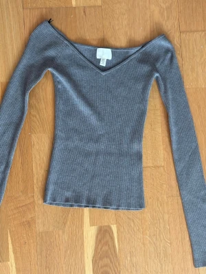 Grå ribbad långärmad topp - Snygg grå ribbad topp med v-ringning och långa ärmar. Modellen är tight och har en stilren, enkel design som passar perfekt till jeans eller kjol. Materialet är mjukt och stretchigt för en bekväm passform.