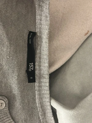 Ljusgrå cardigan från 157 - Ljusgrå cardigan från 157 med ribbade muddar och knappar framtill. Klassisk och enkel design som passar till det mesta. Tillverkad i mjukt material för en bekväm känsla.