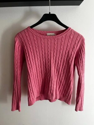 Rosa kabelstickad tröja Holly & Whyte - Säljer en rosa kabelstickad tröja från Holly & Whyte by Lindex. Tröjan har rund halsringning, långa ärmar och ett klassiskt kabelmönster. Perfekt för dig som gillar en färgglad och mysig stil.