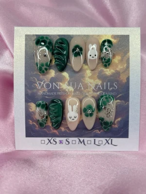 MiffyClover (S);Medium Almond - Unika handgjorda press-on naglar i medium lång mandelform. Designen har mörkgröna cateye, vita kaniner(Miffy), blommor och prickiga detaljer på en nude bas. Miffy/silver motiv och handmålad 3D-effekter ger en lekfull och trendig look. Perfekt för dig som vill sticka ut med söta och kreativa naglar.S: 15 mm, 11,5 mm, 12 mm, 11 mm, 9 mm 