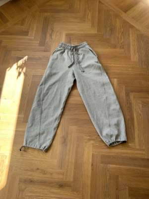 Grå mjukisbyxor - Säljer ett par grå mjukisbyxor med resår i midjan och dragsko för skön passform. Byxorna har sidofickor och en bakficka, samt resår vid bensluten. Perfekta för chill dagar eller när du vill vara bekväm.       Storlek xs i vuxenstorlek        Ordinarie pris: 380kr