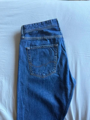 Jeans (Jack & Jones)  - Blåa jeans från Jack & Jones i modellen Loose/Chris. Jeansen har en klassisk design med fyra knappgylf. Säljs till 85% lägre pris än originalpriset. W: 32 / L: 32