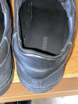 Svarta sneakers från Axel Arigato - Stilrena svarta sneakers från Axel Arigato med lågt skaft. Skorna är tillverkade i läder och mocka, med diskret branding på innersulan. Perfekta för dig som gillar minimalistisk och clean design.