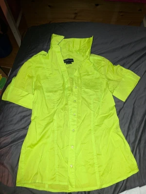 Neongul skjorta med kort ärm - Snygg neongul skjorta från Lake Line med korta ärmar och markerad krage. Skjortan har knappar hela vägen framtill och två bröstfickor. Perfekt för dig som vill sticka ut med en färgstark look.