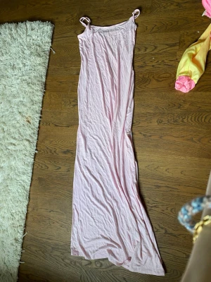 Långt ljusrosa nattlinne med smala band - Säljer ett långt nattlinne i ljusrosa med smala axelband och rak passform. Materialet ser mjukt och tunt ut, perfekt för att chilla hemma eller sova i. Enkel och stilren design utan synliga detaljer eller mönster.