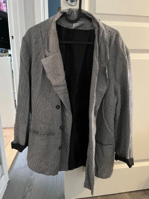 Rutigt kavaj från Christian Cordell - Snygg svartvit rutmönstrad kavaj från Christian Cordell. Klassisk modell med två knappar framtill, fickor och helsvart foder. Perfekt oversized look och tidlös design som passar till många olika stilar.