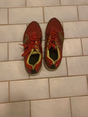 Röda Saucony sneakers mesh - Snygga röda sneakers från Saucony med ventilerande mesh-överdel och gula detaljer. Skorna har vita och limegröna sulor samt klassisk logga på sidan. Perfekta för dig som gillar sportig stil och vill ha bekväma skor till vardags.