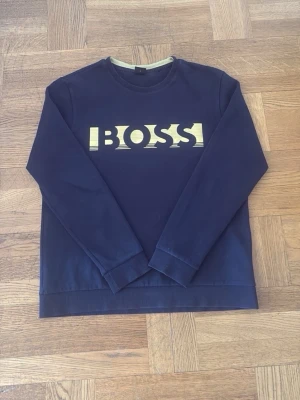 Mörkblå BOSS sweatshirt med tryck - Snygg mörkblå sweatshirt från BOSS med stort gult logotryck på bröstet. PRIS KAN DISKUTERAS 