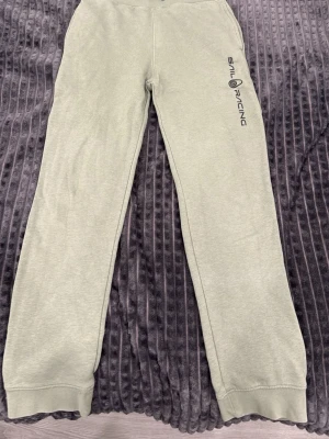 Ljusgröna mjukisbyxor Sail Racing - Mysiga ljusgröna mjukisbyxor från Sail Racing med tryckt logga längs ena benet. Byxorna har resår i midjan och muddar vid bensluten. Perfekta för chill dagar eller när du vill vara bekväm. Tillverkade i mjukt material.