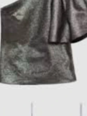 Silver one shoulder topp - Snygg metallic silverfärgad topp med one shoulder-design och stor volangdetalj över axeln. Perfekt för dig som vill sticka ut med en trendig och glittrig look. Materialet har en skimrande finish som fångar ljuset.